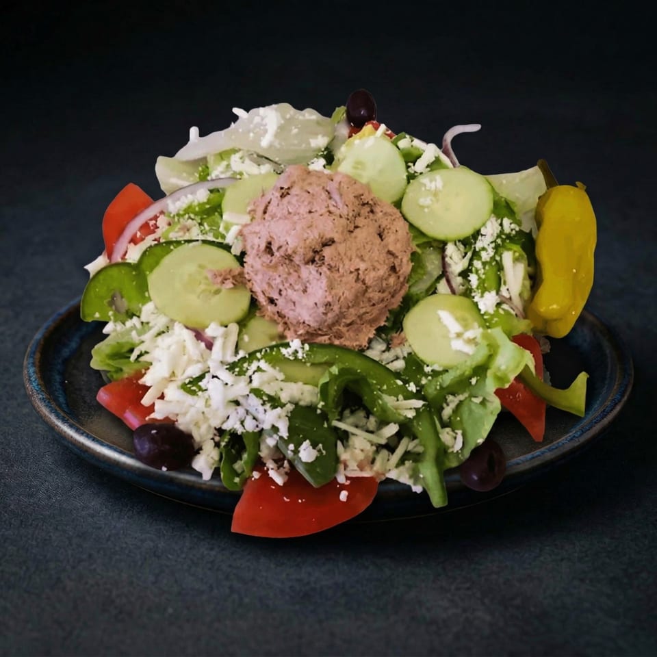 Greek salad with lettuce, tomatoes, cucumbers, feta, olives, green peppers, and a scoop of tuna salad.