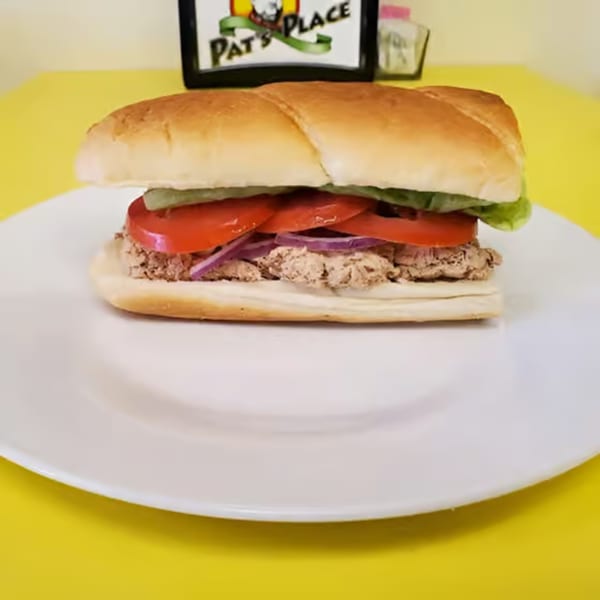 A Pat's Place sub sandwich with tuna, lettuce, tomatoes, and red onions on a white plate.