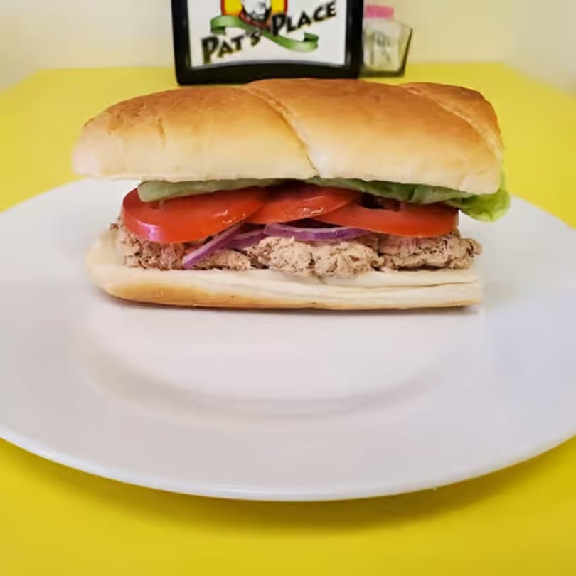 A Pat's Place sub sandwich with tuna, lettuce, tomatoes, and red onions on a white plate.